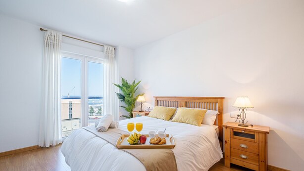 Camera d'albergo con un letto grande, un comodino in legno con una lampada, un vassoio con prodotti per la colazione e vista sulla città dalla finestra.