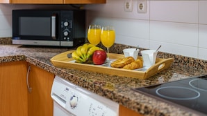 Una cucina con forno a microonde, tostapane e un vassoio con prodotti per la colazione, tra cui banane, una mela, croissant e succo d'arancia.