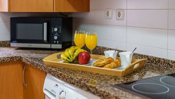Una cocina con microondas, tostadora y una bandeja con alimentos para el desayuno, incluyendo plátanos, una manzana, croissants y jugo de naranja.