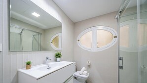 Et moderne badeværelse med et stort spejl, to runde vinduer, en vask, et toilet og en brusekabine i glas.
