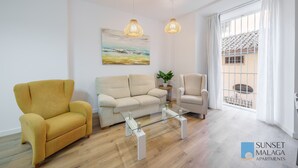 En moderne stue med en gul lænestol, en beige sofa og et glasbord. Der er et billede på væggen og en potteplante på et sofabord.