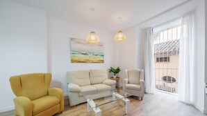 Una sala de estar moderna con un sillón amarillo, un sofá color beige y una mesa de centro de vidrio. Hay un cuadro en la pared y una planta en maceta sobre una mesita auxiliar.
