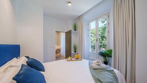 A hotel room with a large bed, a blue headboard, a breakfast tray on the bed, and a view of greenery outside. - Sunset Malaga Apartments - Alameda Apt 1 (Málaga)
