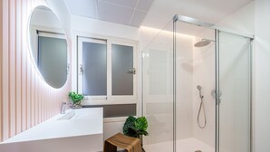 A modern bathroom with a glass shower enclosure, a white sink with a mirror, and a small wooden stool. - Sunset Malaga Apartments - Alameda Apt 1 (Málaga)