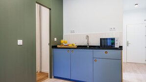 A compact kitchen with blue cabinets, a black countertop, and a microwave. There are two white switches on the wall and a small window above the sink. - Sunset Malaga Apartments - Alameda Apt 1 (Málaga)