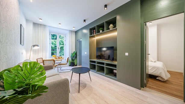 A modern living room with a sofa, dining table, and a TV on a built-in shelf. - Sunset Malaga Apartments - Alameda Apt 1 (Málaga)