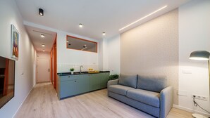 Un salon moderne avec un canapé gris, une table basse en bois et un coin cuisine comprenant un évier et un plan de travail.