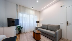 En moderne stue med et fladskærms-tv, en grå sofa, et lille træsofa-bord og en potteplante.