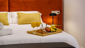 En pænt redt seng med et bakke med morgenmad, herunder croissanter, æbler, bananer og appelsinjuice.