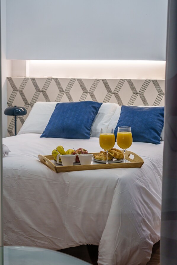 Un lit bien fait, avec un plateau de petit-déjeuner comprenant des fruits, des croissants et du jus d’orange.