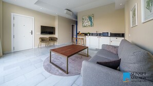 Un salon moderne avec un canapé, une table basse et un téléviseur. Il y a également un coin cuisine équipé d’un four à micro-ondes et d’un évier.