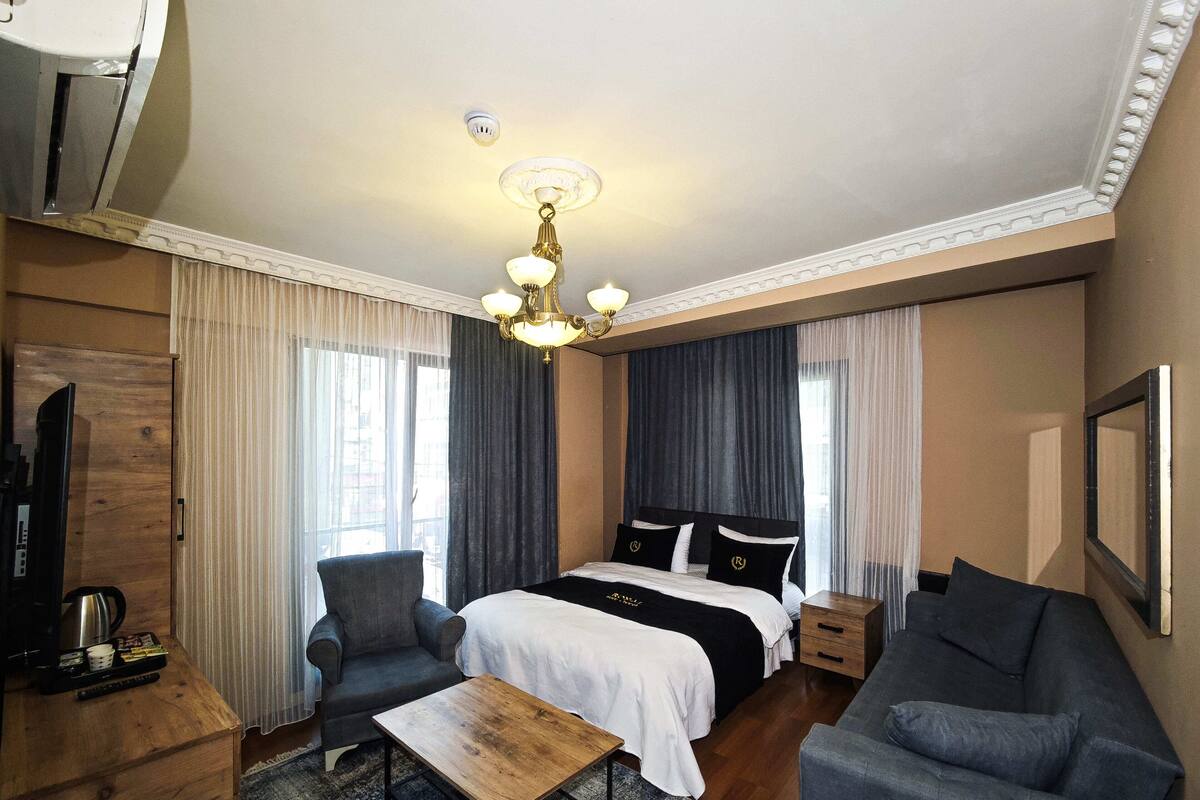 A hotel room with a large bed, two armchairs, a wooden coffee table, a TV, and a minibar.