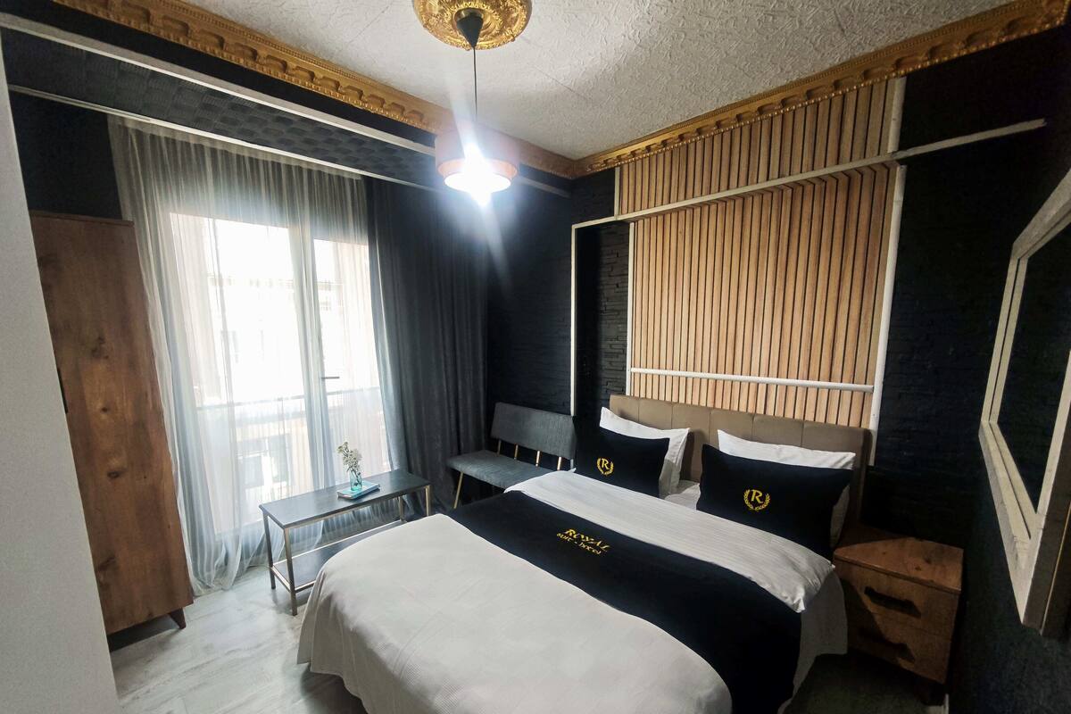 A hotel room with a large bed, bedside tables, a desk, and a view of the outside through a window with curtains.