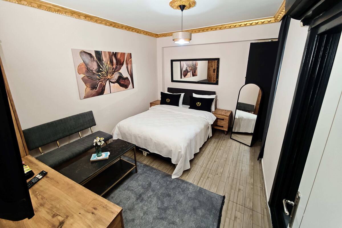 A modern bedroom with a bed, bedside tables, a desk, and artwork on the walls.