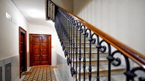 A staircase with a wooden handrail and black wrought iron balusters, leading to a wooden door at the bottom. - Anthony 47 (Rome)