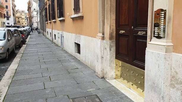 A narrow street with parked cars and a building with a large wooden door and a brass knocker. - Anthony 47 (Rome)