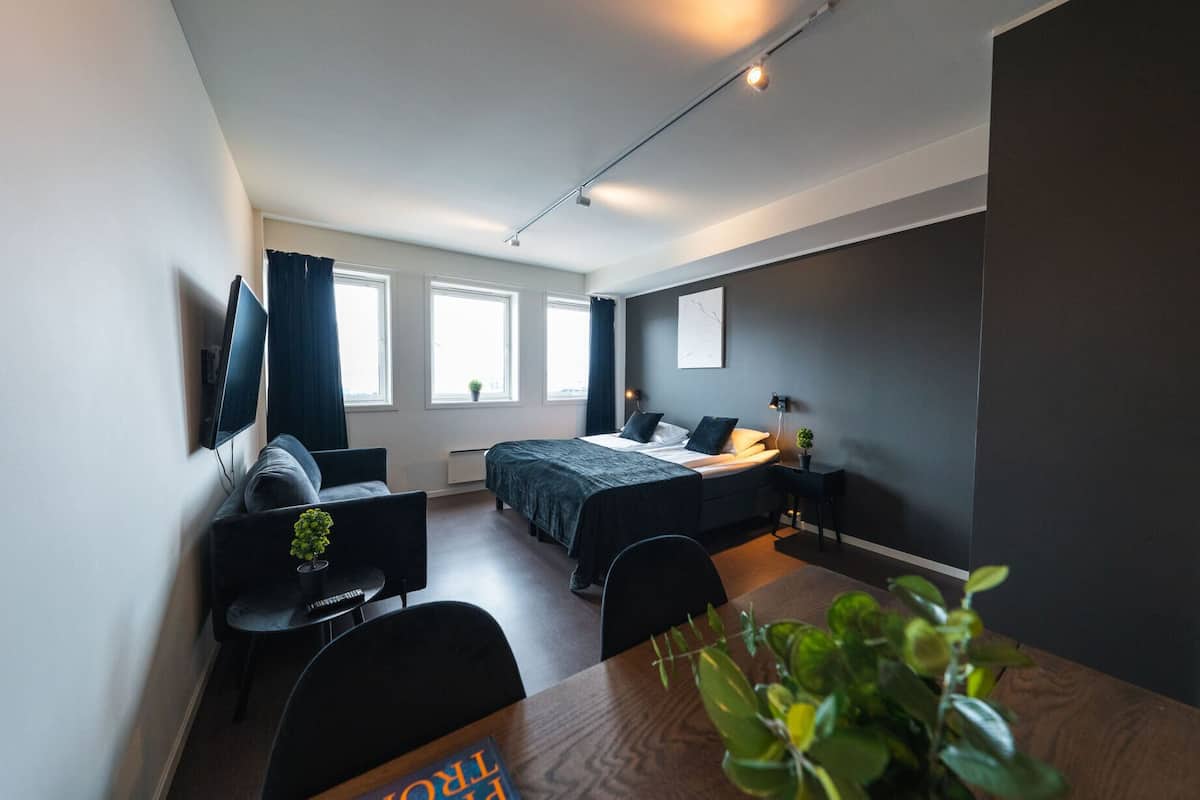 A modern hotel room with a bed, a desk, a chair, and a TV.