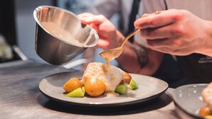 Eine Person gibt Soße über ein Gericht mit Kartoffeln und Gemüse.