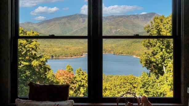 Ein Zimmer mit großem Fenster und Blick auf einen See, der von Bergen und Bäumen umgeben ist.