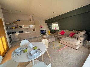 A modern living room with a dining area, a sofa set, and a kitchen in the background. - Lower Mill Estate Penthouse Apartment with Spa Access included (Somerford Keynes)
