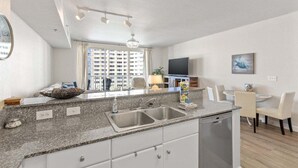 A modern kitchen with granite countertops, a built-in dishwasher, and a dining area with a round table and chairs.