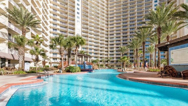 A large indoor swimming pool with palm trees and lounge chairs, surrounded by high-rise hotel buildings.