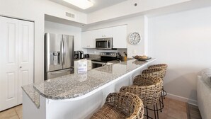 A modern kitchen with white cabinetry, stainless steel appliances, a granite countertop, and wicker bar stools.