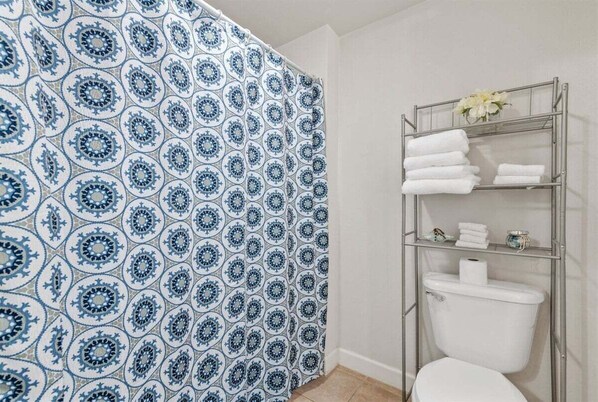 Un baño con cortina de ducha estampada, un perchero metálico con toallas dobladas y un inodoro.