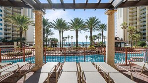 A pool area with lounge chairs, palm trees, and a view of the ocean.