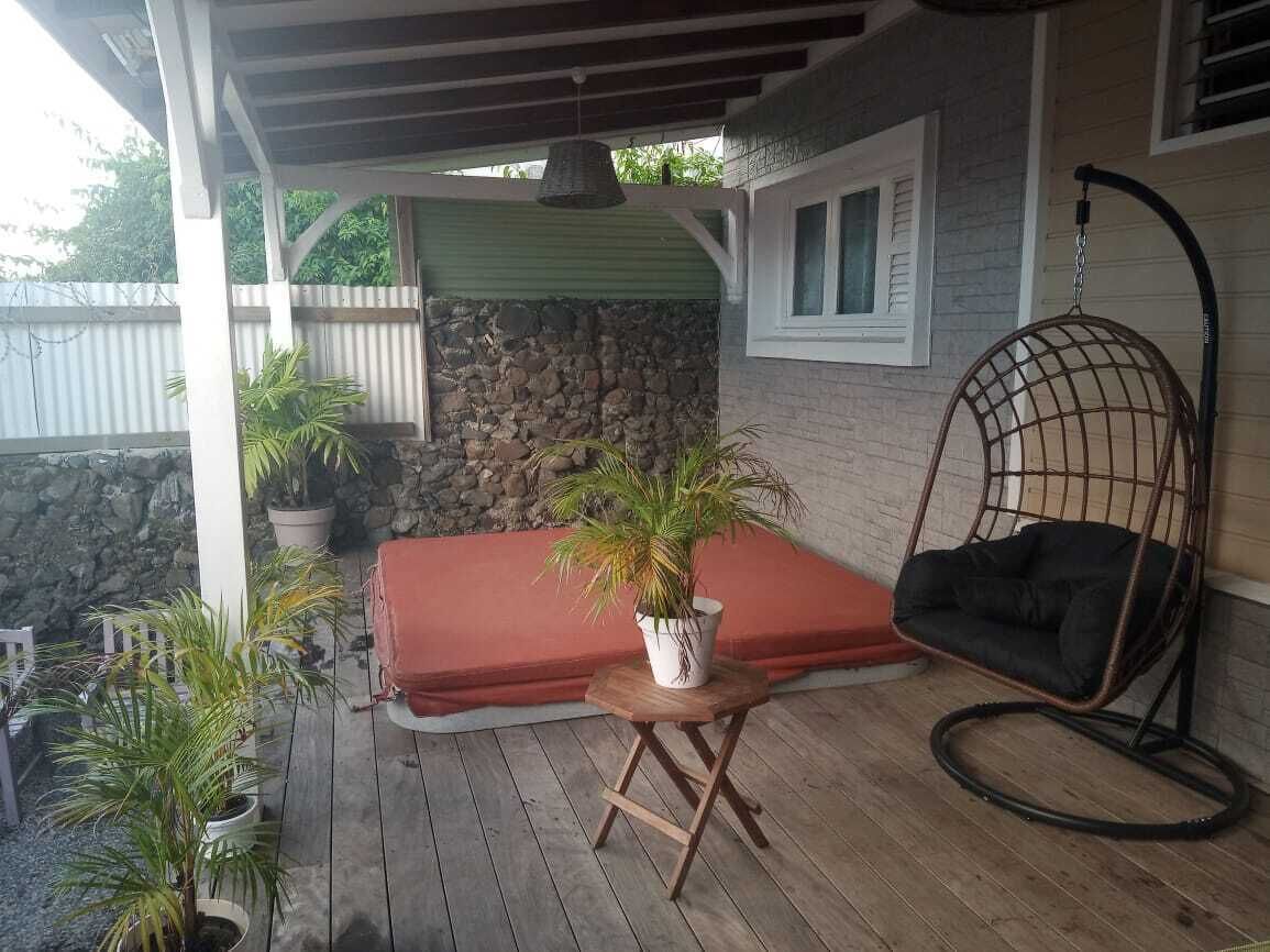 A covered outdoor seating area with a cushioned bench, a hanging chair, and potted plants.