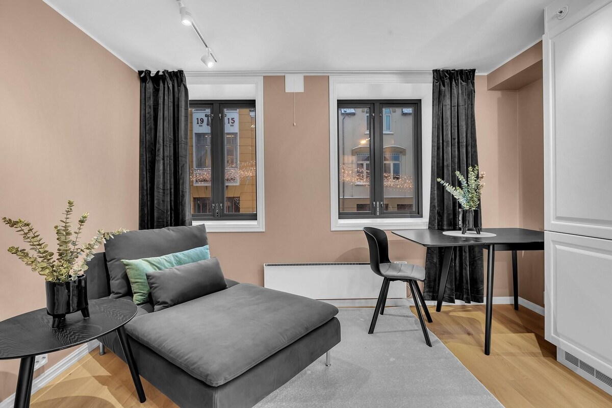 A modern, compact living space with a grey sofa, a small black table, a chair, and a potted plant.