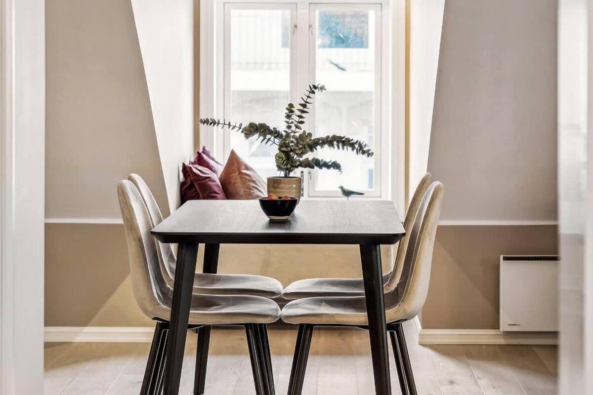 A dining area with a table, chairs, a potted plant, and a window.