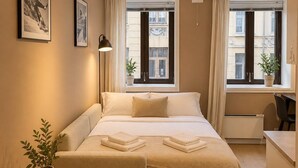 A modern bedroom with a bed, bedside tables, a small round table with a plant, and a view of the city through large windows. - 70 Degrees North Apartment (Tromsø)