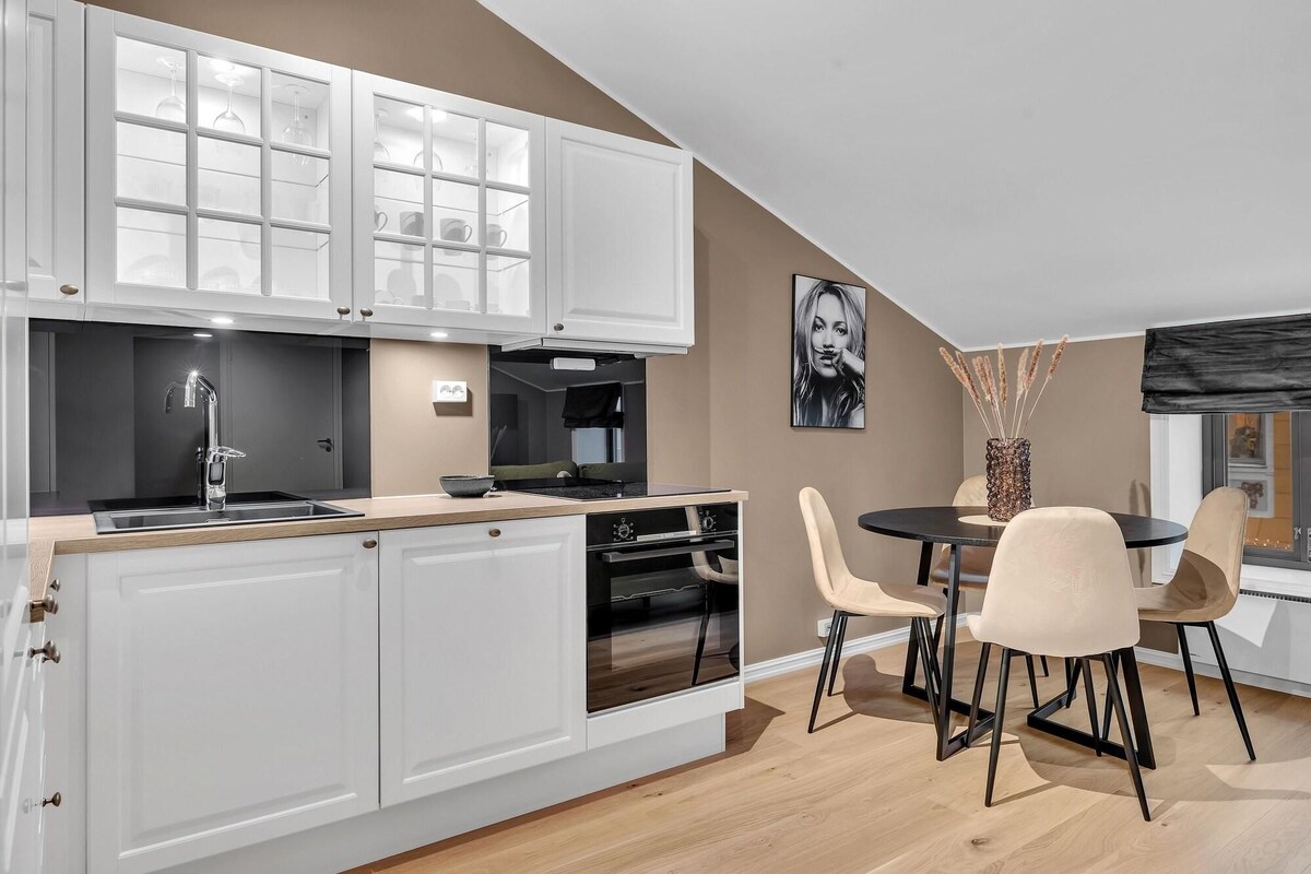 A modern kitchen with white cabinetry, a built-in oven, and a dining area with a round table and chairs.