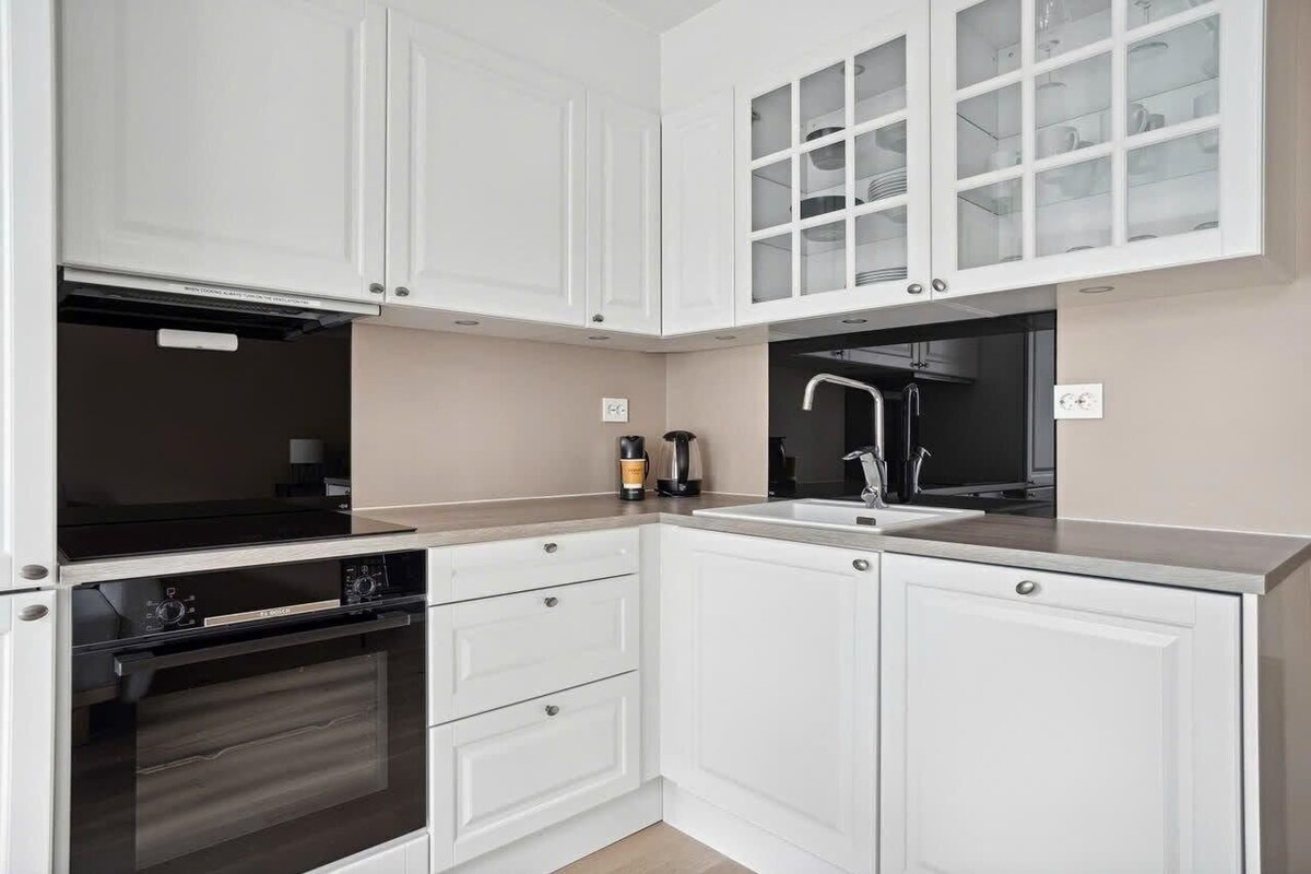 A modern kitchen with white cabinetry, a black stove, and a sink.