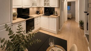 A modern kitchen with white cabinets, a dining area with a table set for two, and a staircase leading to an upper level. - 70 Degrees North Apartment (Tromsø)