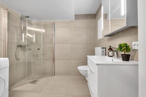 A modern bathroom with a glass shower enclosure, a toilet, a sink with a mirror, and a potted plant. - 70 Degrees North Apartment (Tromsø)