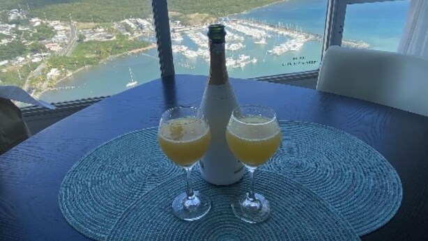 Un tavolo con una bottiglia e due bicchieri di una bevanda gialla, con vista sulla costa sullo sfondo.