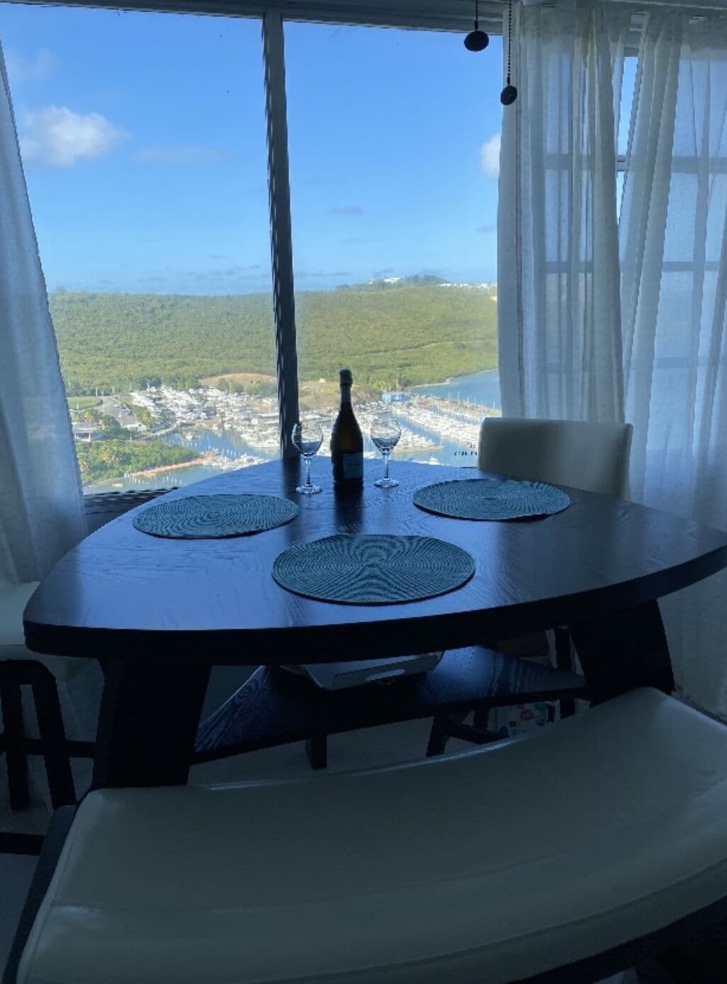 Une table à manger avec une bouteille et des verres, donnant sur un paysage côtier.