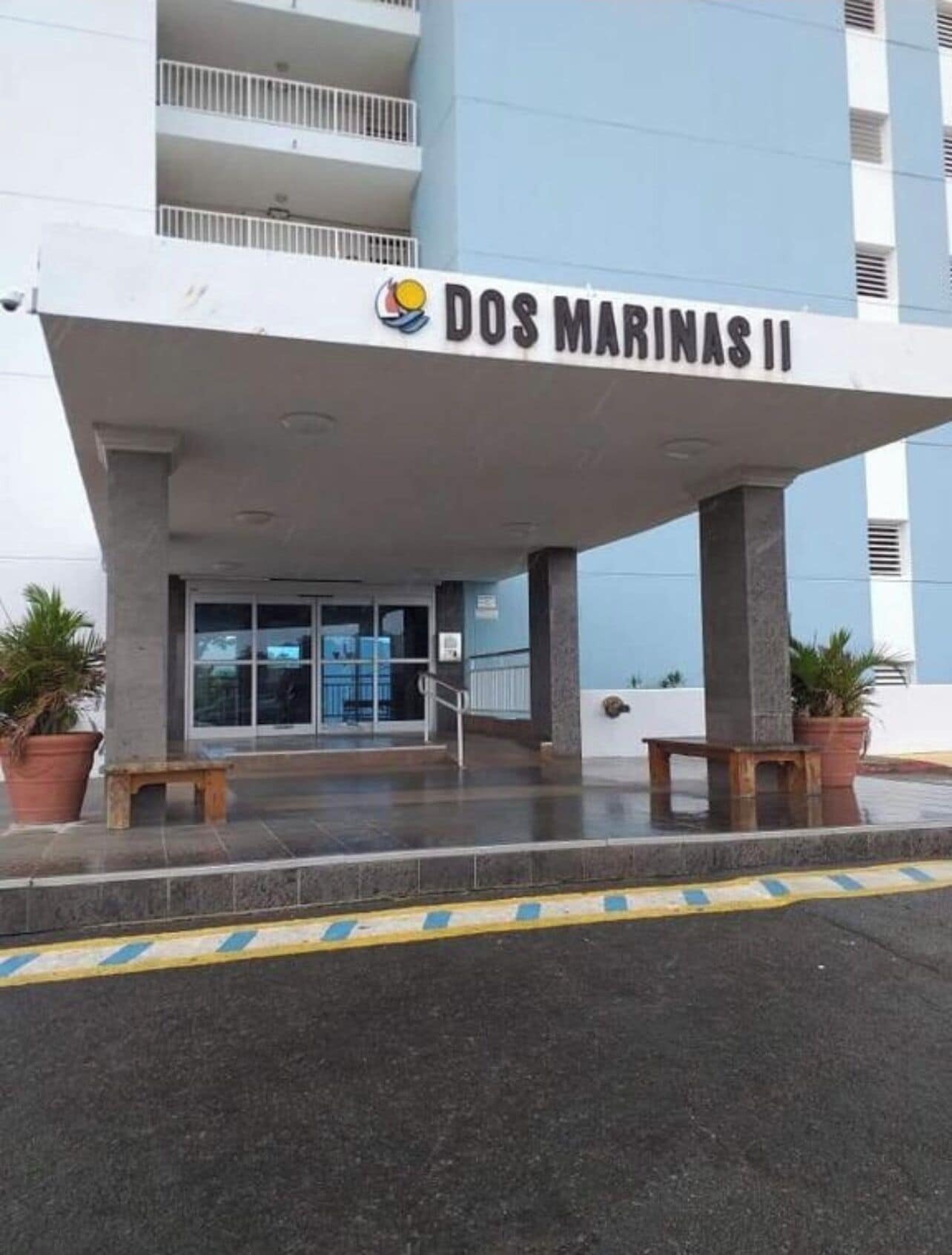 La entrada a Dos Marinas II, con un vestíbulo techado, plantas en macetas y un banco.