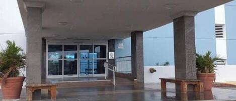 La entrada a Dos Marinas II, con un vestíbulo techado, plantas en macetas y un banco.