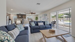 A spacious living area with a dark blue sofa set, a wooden coffee table, and a view of the backyard through large sliding glass doors.