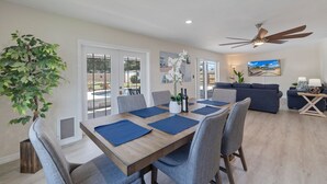 A modern living room with a dining area, a ceiling fan, and a view of the outdoors.