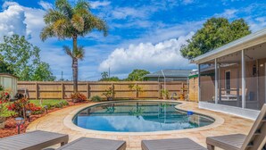 A backyard with a swimming pool, wooden deck, and lounge chairs.