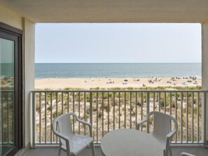 A balcony with two white plastic chairs and a small table, overlooking a beach with people and umbrellas. - Direct ocean front 2 Bedroom 2 Bath with pool (Ocean City)