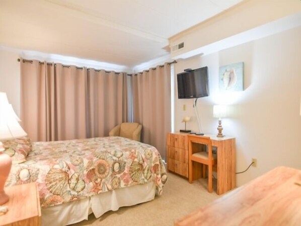 A hotel room with a bed, a desk, a chair, a TV, and curtains. - Direct ocean front 2 Bedroom 2 Bath with pool (Ocean City)