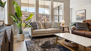 Un salón con un sofá color crema, una mesita de centro y un ventanal con vistas a un paisaje rocoso.