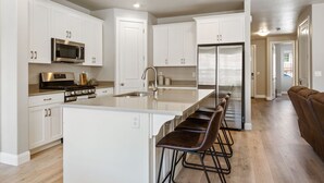Una cocina moderna con muebles blancos, electrodomésticos de acero inoxidable y una isla central con taburetes de bar.