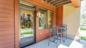 Exterior de madera con puerta corredera de vidrio, un patio con sillas de metal y una pequeña mesa.