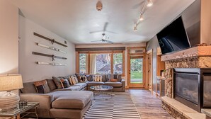 Una sala de estar moderna con un sofá modular, una mesa de centro de vidrio, una chimenea y un televisor montado en la pared.